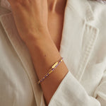 Gold chain bracelet with purple beaded strand and rectangular bar charm on a wrist
