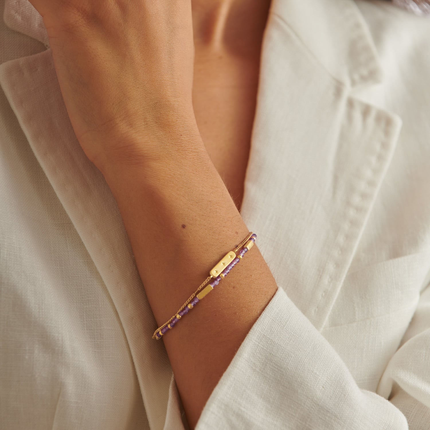 Gold chain bracelet with purple beaded strand and rectangular bar charm on a wrist