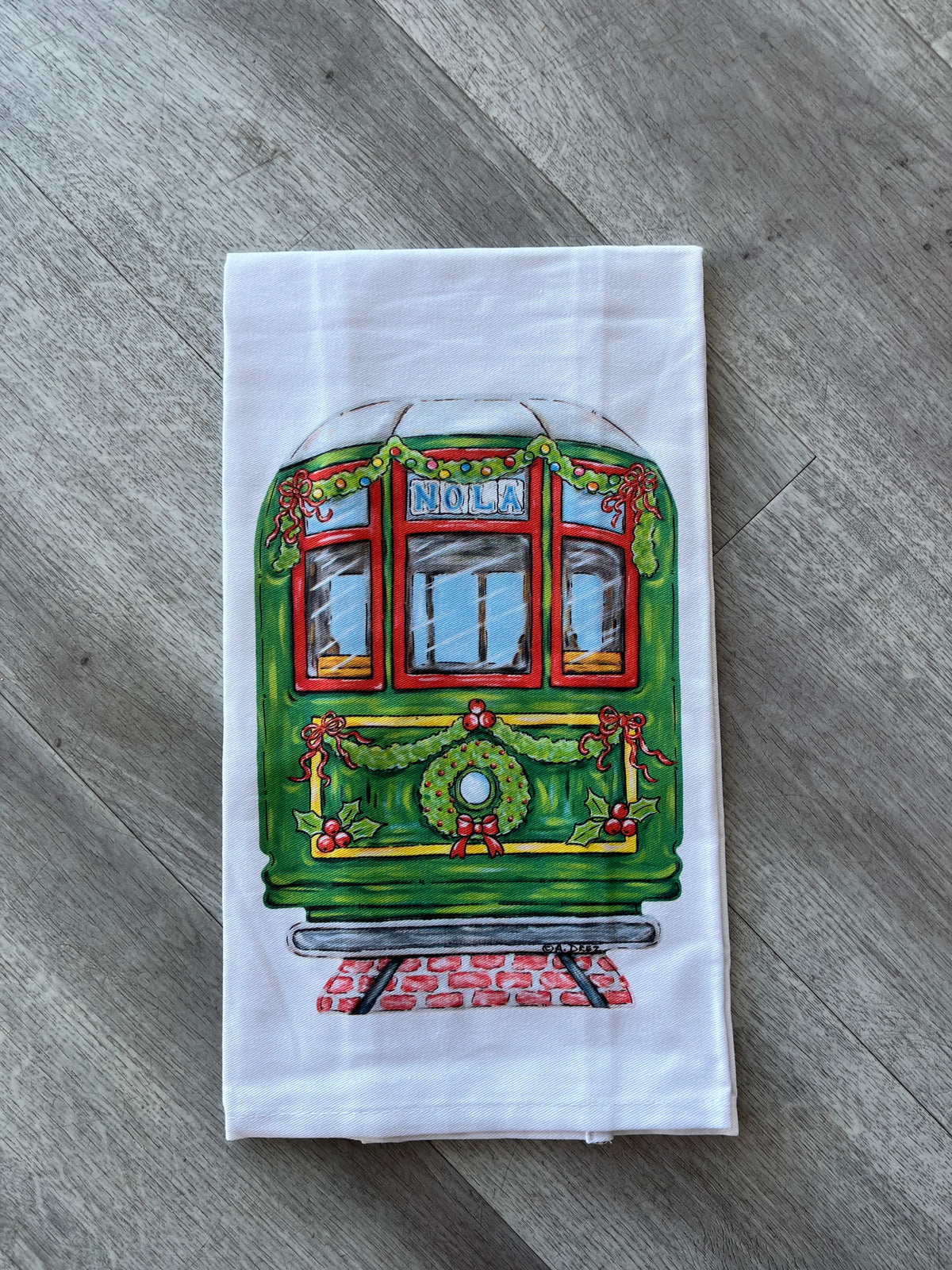 White towel printed with a green NOLA streetcar decorated with a Christmas wreath and garland