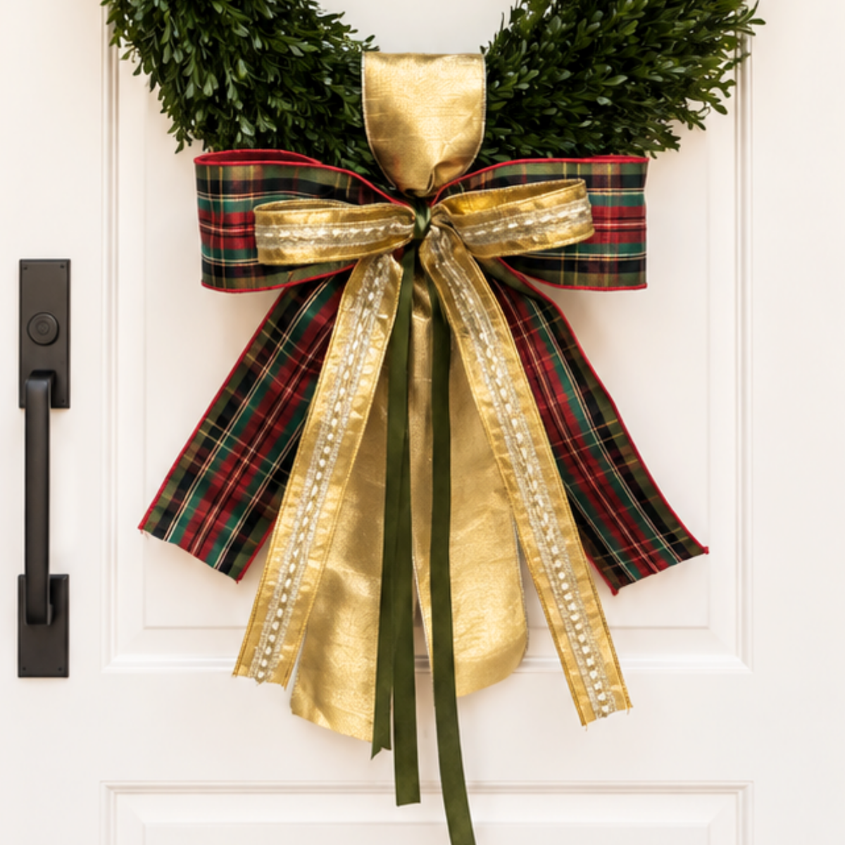 Bow of red and green tartan, gold satin, gold trim and dark green ribbons on a boxwood wreath