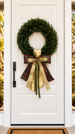 White front door with a boxwood wreath and a tartan plaid and gold ribbon bow