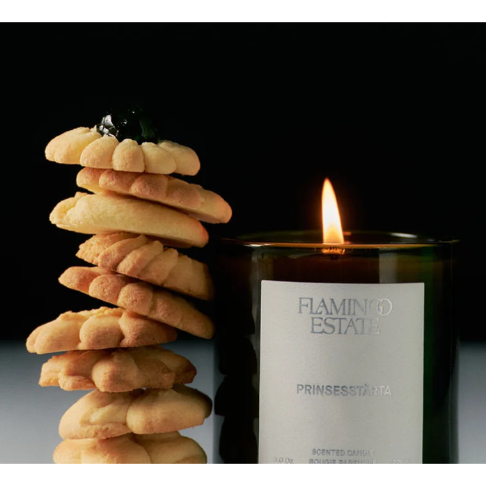 Lit Flamingo Estate Prinsesstarta candle beside a stack of cookies