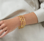 Three gold bangles with bee motifs worn on a wrist
