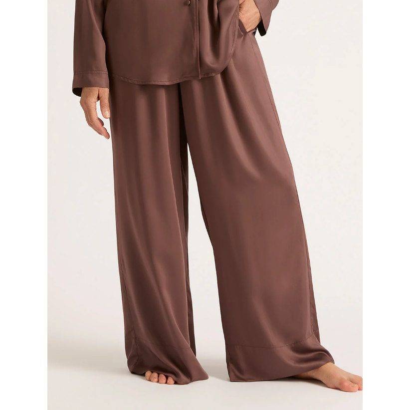 A person standing wearing brown wide-leg sleep pants.