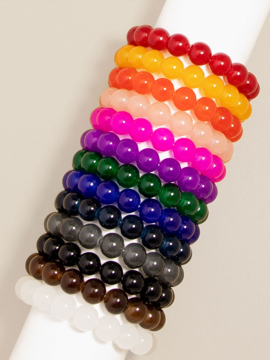 Smooth round beaded bracelets in a vibrant rainbow-to-neutral gradient stacked on a white display