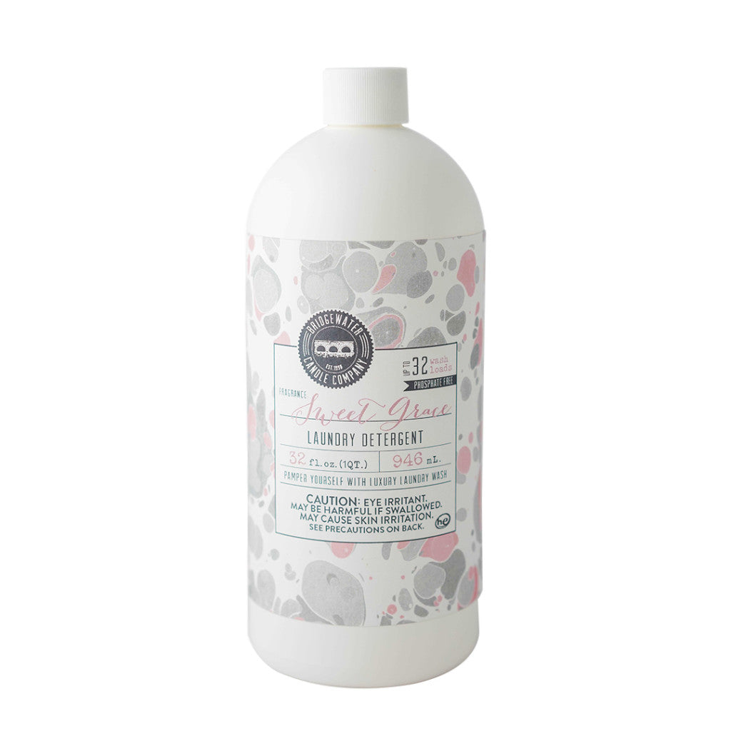 Product photograph of a Bridgewater Candle Company Sweet Grass laundry detergent bottle on a white background featuring a gray and pink marbled label, a white ribbed cap, and an iconic circular bridge logo