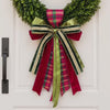 Green boxwood wreath on a white front door shown with a series of holiday sashes and bows