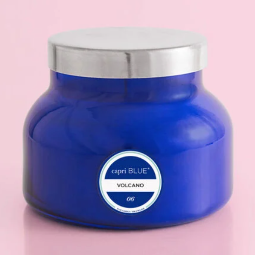 A blue candle labeled 'VOLCANO' by Capri Blue, placed on a pink surface.