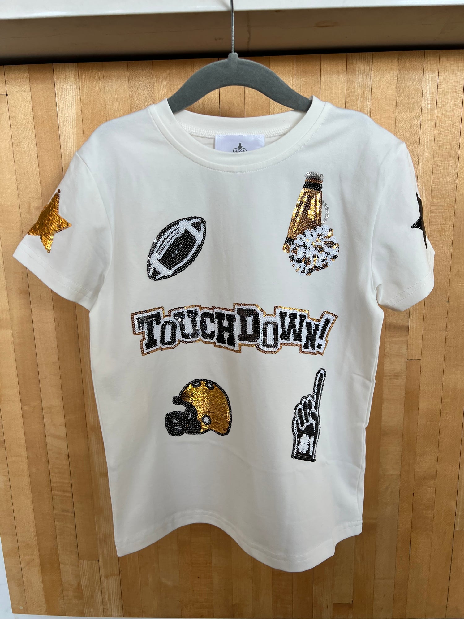 A white short-sleeve adult shirt with black and gold sequins featuring NFL touchdown graphics and the text 'TOUCHDOWN!' displayed.