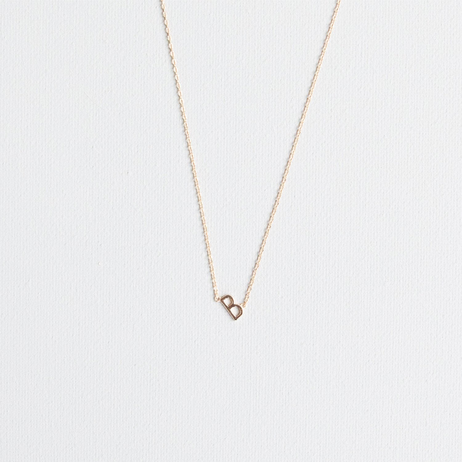 Jewelry delicate gold initial 'b' necklace on a textured white background