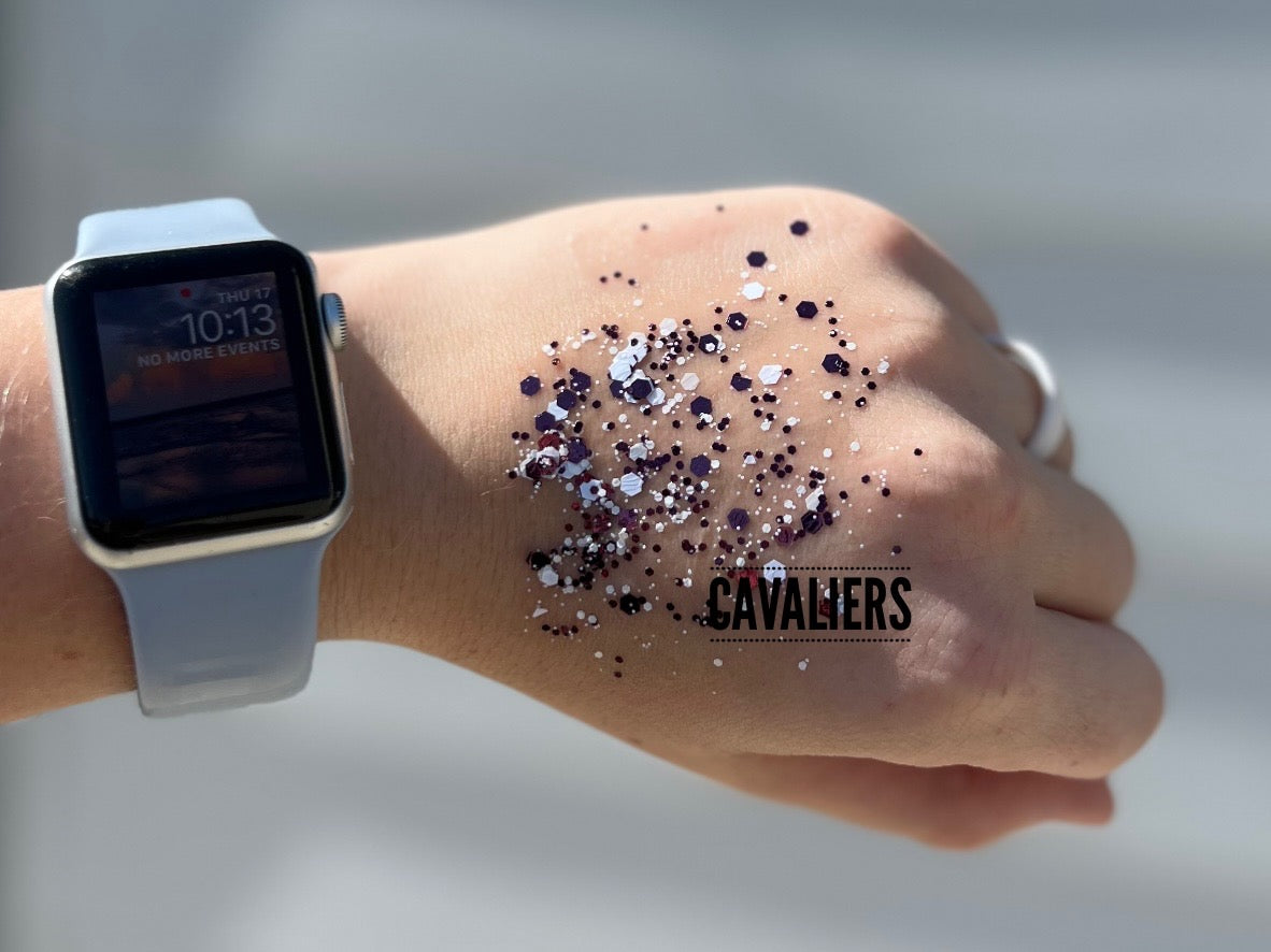Photograph of a hand wearing a light blue Apple Watch displaying 10:13 and a sunset image, adorned with scattered purple, white, and black glitter, and a 'CAVALIERS' text overlay