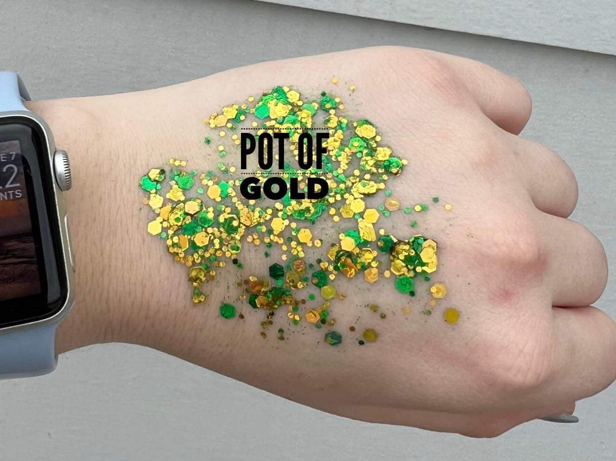 Close-up of a hand adorned with vibrant green and gold hexagonal glitter with an overlay of the words POT OF GOLD and a light blue Apple Watch on the wrist
