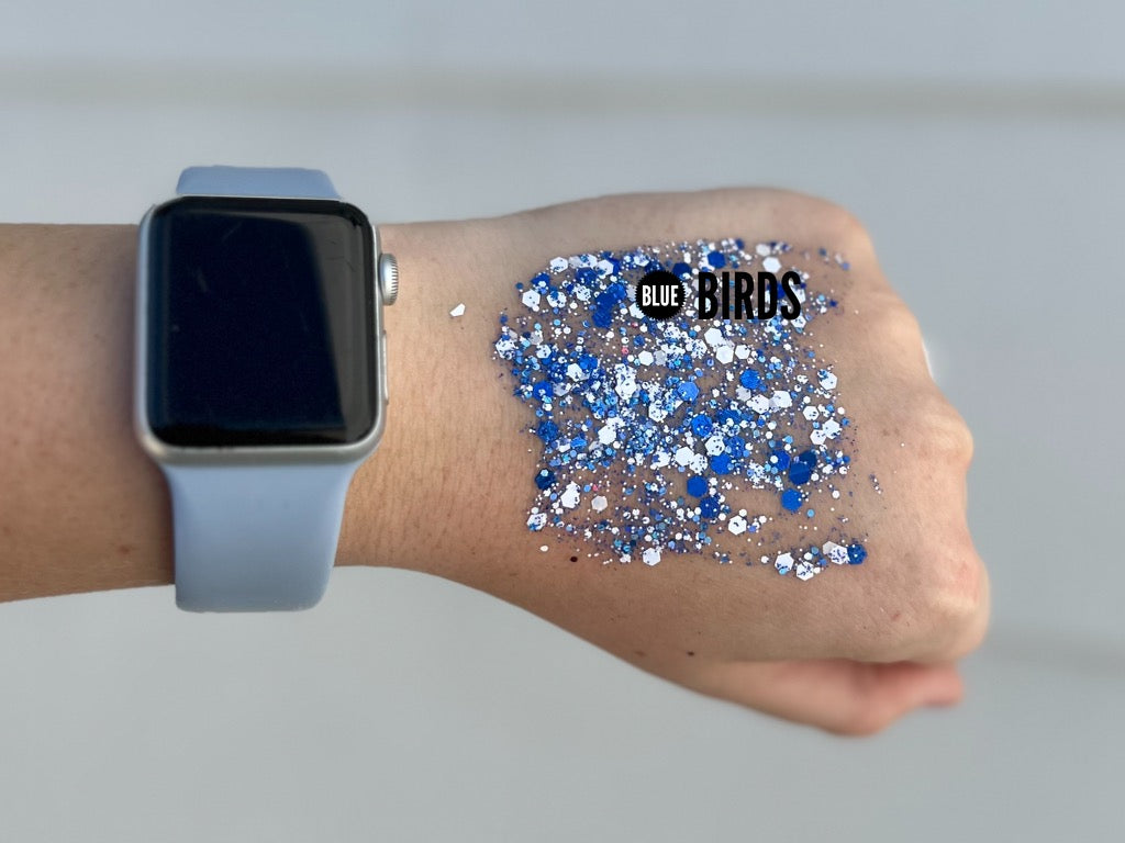 A close-up shot of a hand wearing a silver Apple Watch with a light blue band, next to a swatch of shimmering multi-sized blue and white chunky BLUE BIRDS glitter