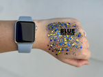 Photography of a hand wearing a light blue Apple Watch band with a large spread of shimmering blue and gold hexagonal glitter and the text BLUE AND GOLD across the back