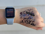 A hand featuring an Apple Watch with a light blue band displaying 10:22, adorned with purple, blue, and black glitter and a prominent black WILDCATS sticker