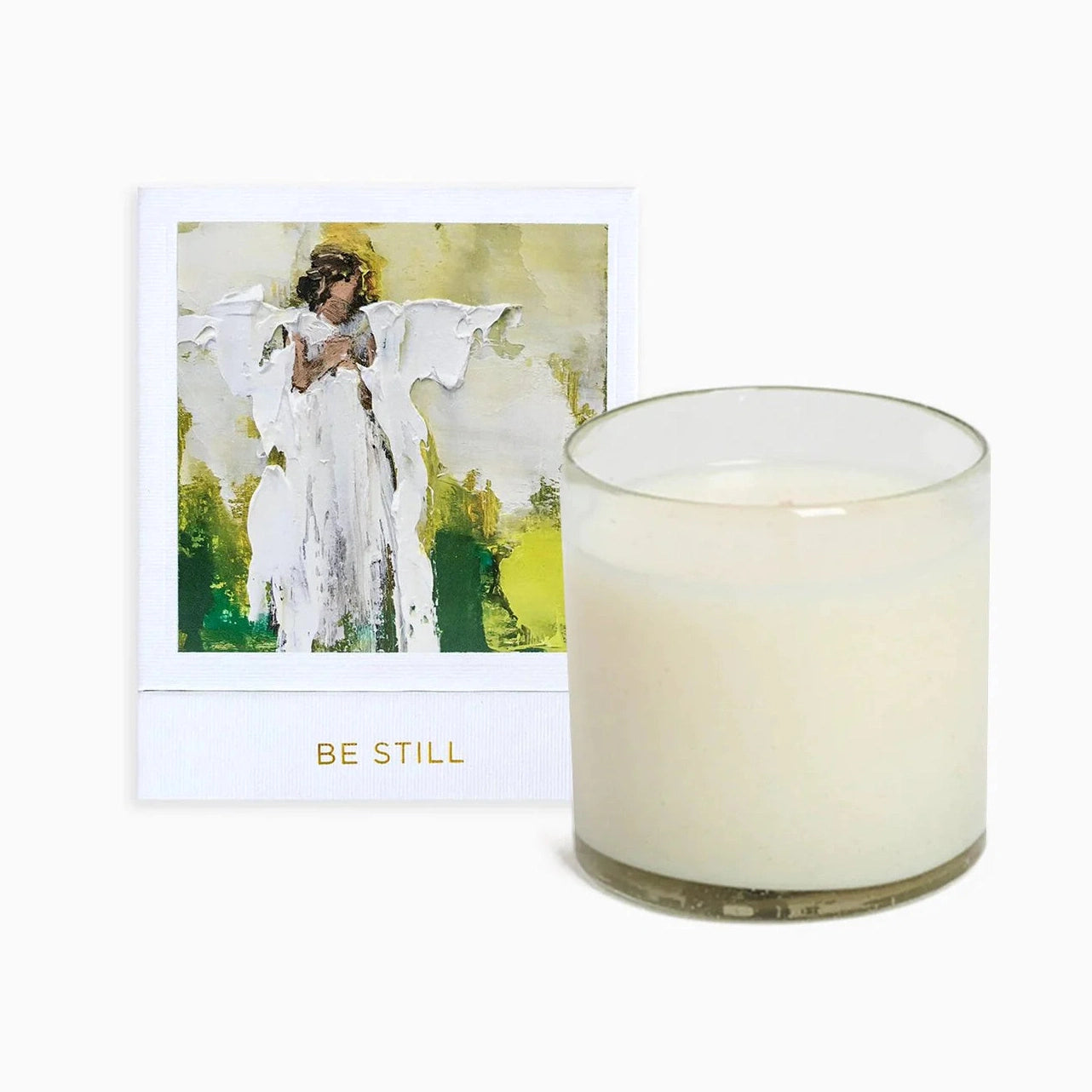 A beige candle with a white label featuring an angel painting, titled 'Be Still'.