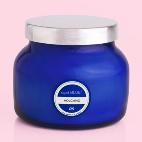 A blue candle labeled 'Volcano' by Capri Blue, with a metallic lid on a pink background.