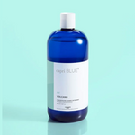 A blue bottle of Capri Blue Volcano laundry detergent on a light turquoise background.