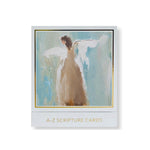 Painted illustration of a stylized angel with brown hair and a flowing light brown gown, featuring broad white wings against a textured blue and cream background, presented in a white frame with a subtle gold border and the words A-Z SCRIPTURE CARDS printed below