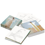 Printed inspirational cards in scattered stacks featuring abstract brushstroke art in soft blues and yellows alongside words like 'Love' and 'Integrity' and scripture verses