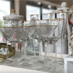 Hammered clear glass drinkware including martini and highball glasses featuring distinctive gold rims on a white display surface