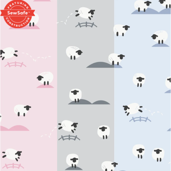 A repeating digital textile pattern depicting playful white cartoon sheep with black faces jumping over stylized fences and standing on small hills across vertical sections colored pink, gray, and light blue, featuring a red SewSafe Construction badge