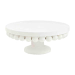 White round cake stand isolated on a white background featuring a smooth top surface and a distinctive scalloped edge of small white spheres above a sturdy pedestal base