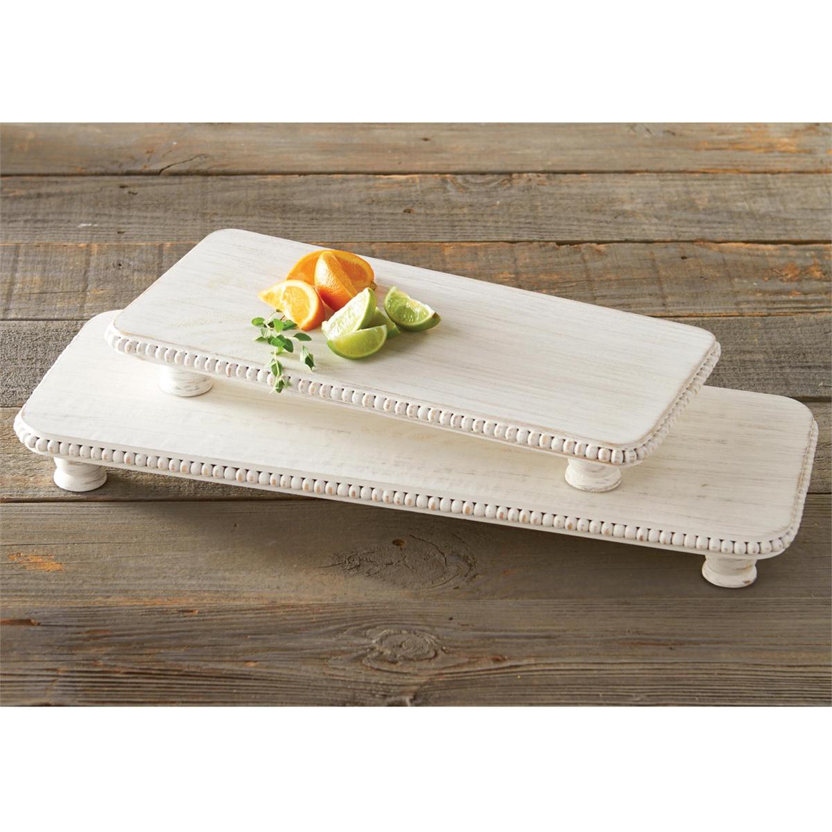 Two distressed white wood beaded pedestal risers on a rustic wooden table displaying colorful orange and lime slices with a fresh green herb sprig