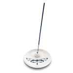 White ceramic circular incense holder decorated with a black stylized dragonfly motif holding an upright black incense stick