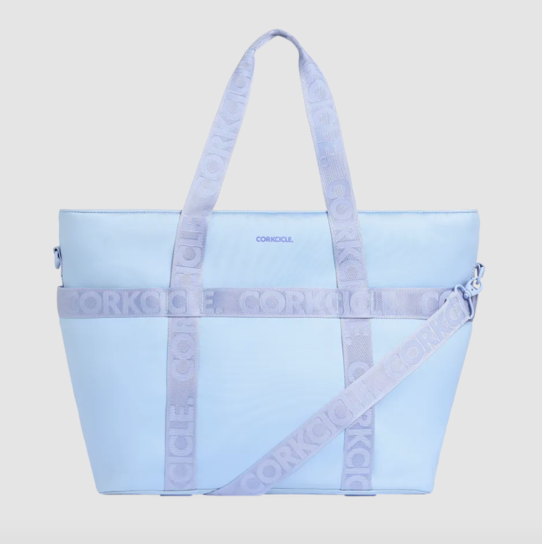 CORKCICLE insulated tote bag in light blue featuring prominent lavender purple straps with repeating embossed CORKCICLE text and a small dark blue brand logo on the front panel