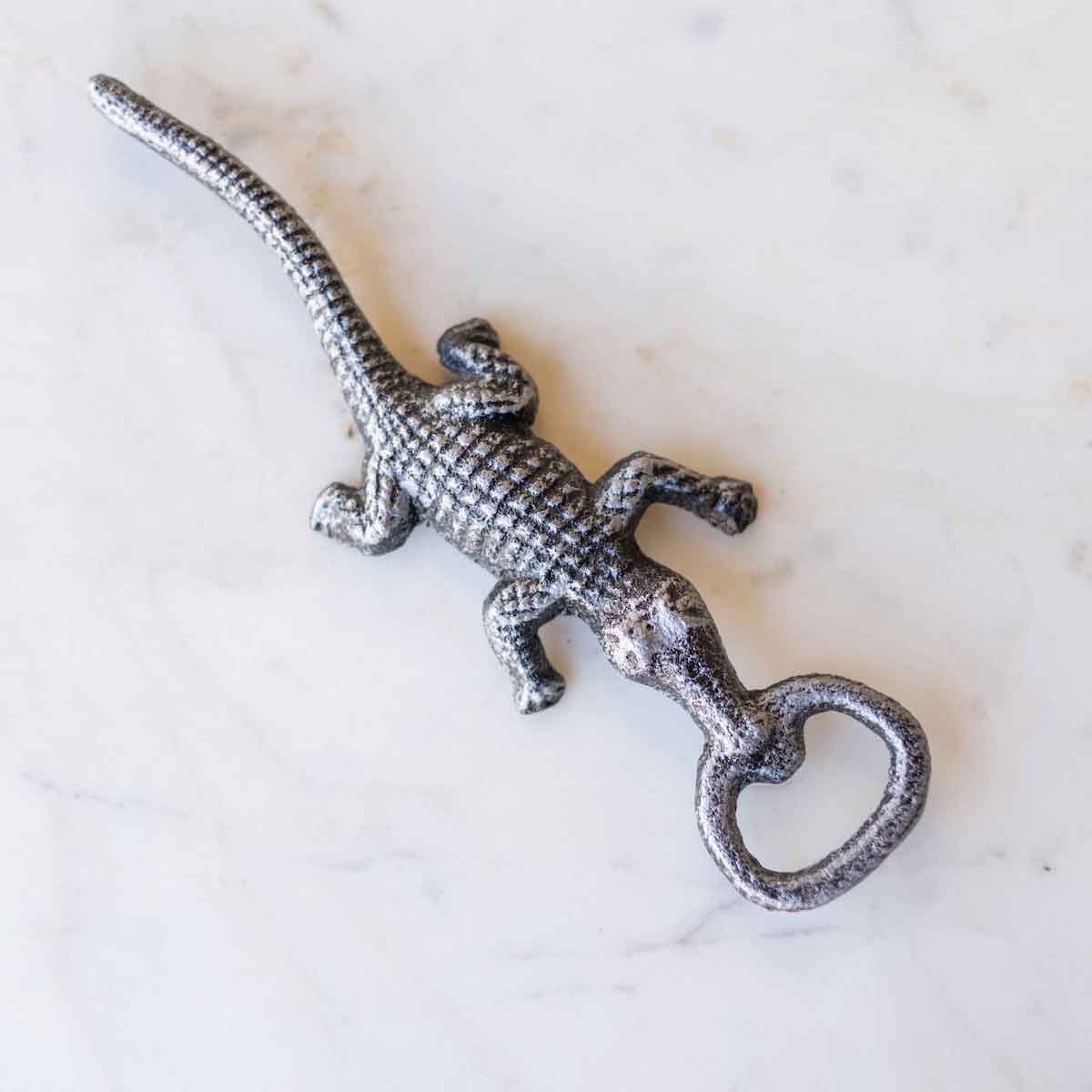 Silver-grey metallic lizard bottle opener featuring a textured scaly body resting on a white marble surface