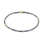 A delicate beaded bracelet featuring alternating tiny blue-purple and gray beads interspersed with small golden metallic beads and one prominent central gold bead