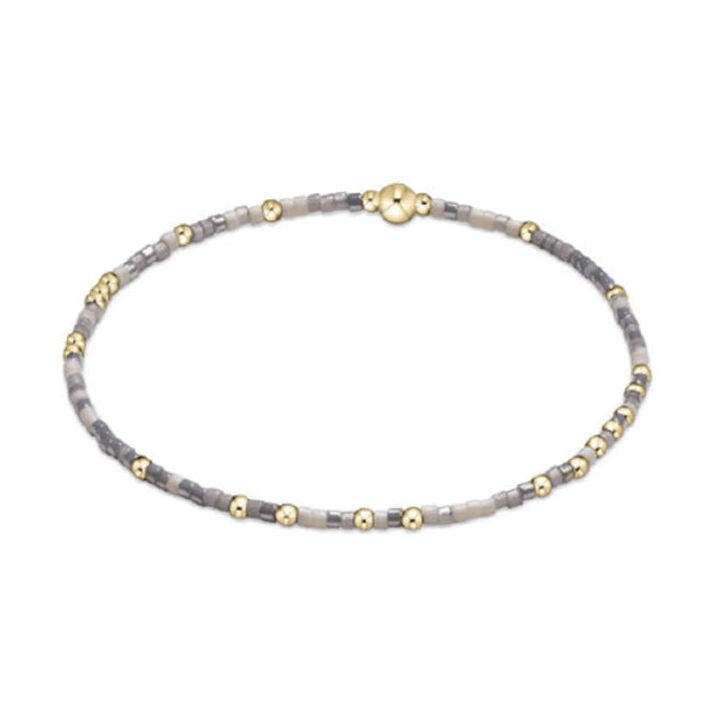 Delicate beaded bracelet featuring small gold spherical beads interspersed with tiny muted grey and beige seed beads and a larger central gold accent bead