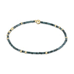 Beaded bracelet featuring alternating dark and light teal square beads interspersed with small gold spheres and secured by a larger gold ball clasp