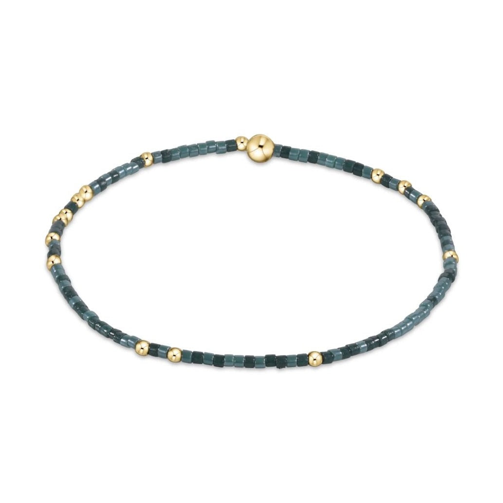 Beaded bracelet featuring alternating dark and light teal square beads interspersed with small gold spheres and secured by a larger gold ball clasp