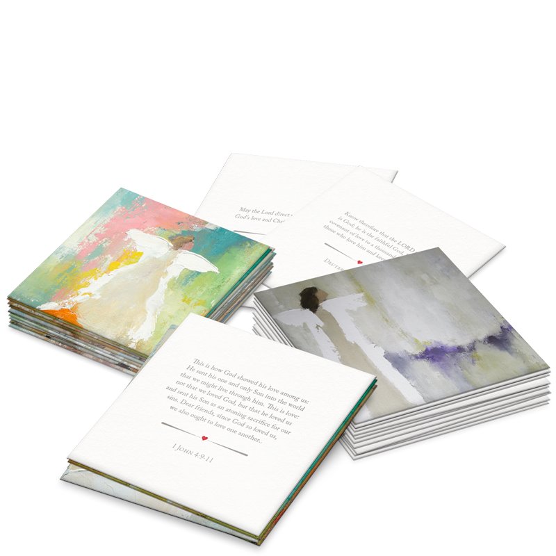 Printed cards featuring multiple stacks of inspirational cards with abstract angel artwork, including one with vibrant pink and teal hues and another with muted purple, alongside visible scripture from 1 John 4:9-11 with a small red heart icon