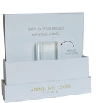 Product display by Anne Neilson Home, a minimalist white cardboard stand designed to display angels, featuring a removable clear acrylic block and elegant gold branding