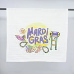 Watercolor illustration by Kate Wilcox on a white towel depicting New Orleans Mardi Gras with vibrant purple lettering, a masquerade mask, green and gold beads, a king cake slice with a baby, and a parade ladder stand