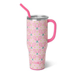 Product photo by Swig Life depicting a pink insulated tumbler with a matching pink handle and straw, decorated with a repeating pattern of crossed pink tennis rackets with green grips and scattered yellow tennis balls