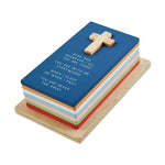 Wooden stacked prayer block featuring a blue top with an embedded light wood cross and white prayer text "Dear God...", with colorful layers in red, green, pink, light blue, and orange on a natural wood base