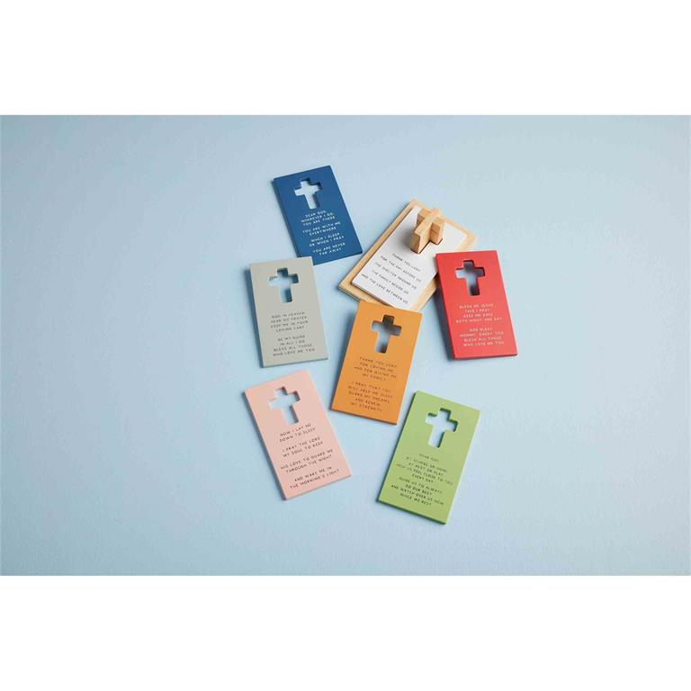 A collection of vibrant cross-cutout prayer cards in shades of blue, peach, orange, red, and green, each featuring different religious texts and scattered on a light blue surface, with one card propped up by a small wooden stand