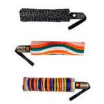 Three folded umbrellas with auto-open buttons: one black and white geometric pattern, one with wavy pink orange green and white stripes, and one with bold vertical blue orange black and tan stripes