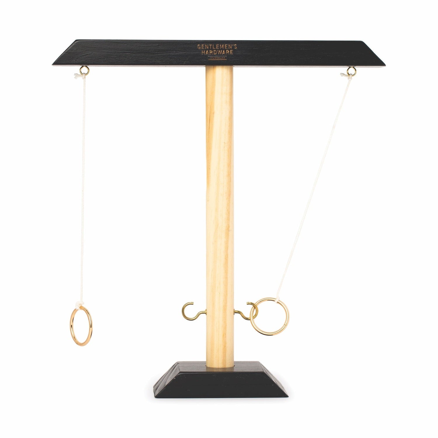 Digital photo by Gentlemen's Hardware showing a wooden ring toss game with a light natural wood central pole, matte black top and base, two brass rings on white strings, and one ring successfully hooked onto a brass hook