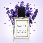 Digital photograph of a clear SAINT English Lavender perfume bottle with a gold-framed white label and black cap, surrounded by vibrant purple lavender sprigs and scattered petals against a soft lavender gradient background