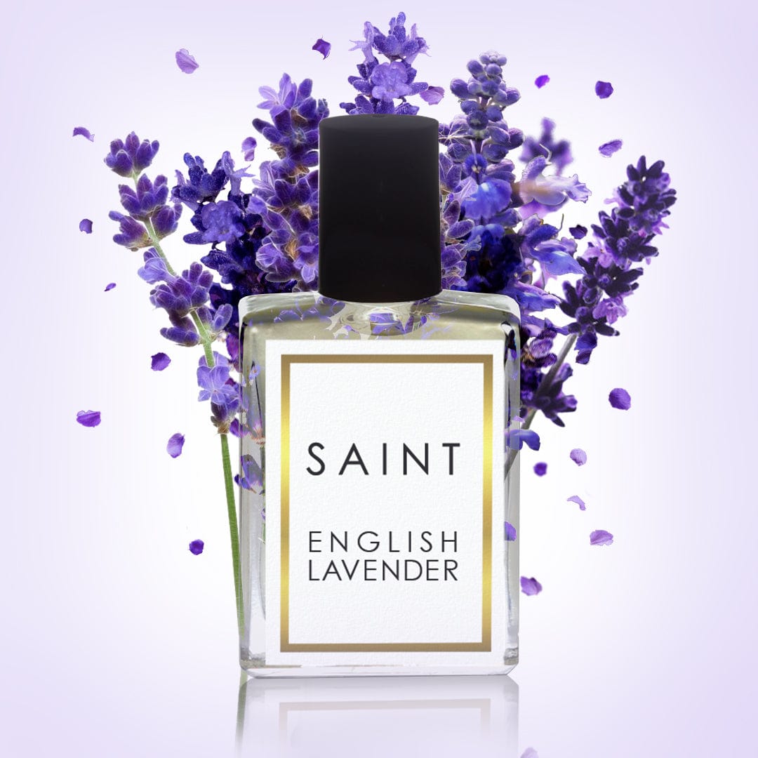Digital photograph of a clear SAINT English Lavender perfume bottle with a gold-framed white label and black cap, surrounded by vibrant purple lavender sprigs and scattered petals against a soft lavender gradient background