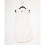 Photograph of a sleeveless white baby sleeping bag with a repeating pink four-petal flower pattern hanging on a black hanger in a clean studio