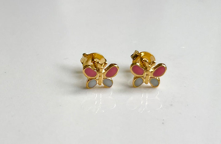 Pair of gold-toned butterfly stud earrings featuring bright pink enamel upper wings and light gray enamel lower wings resting on a clean white surface