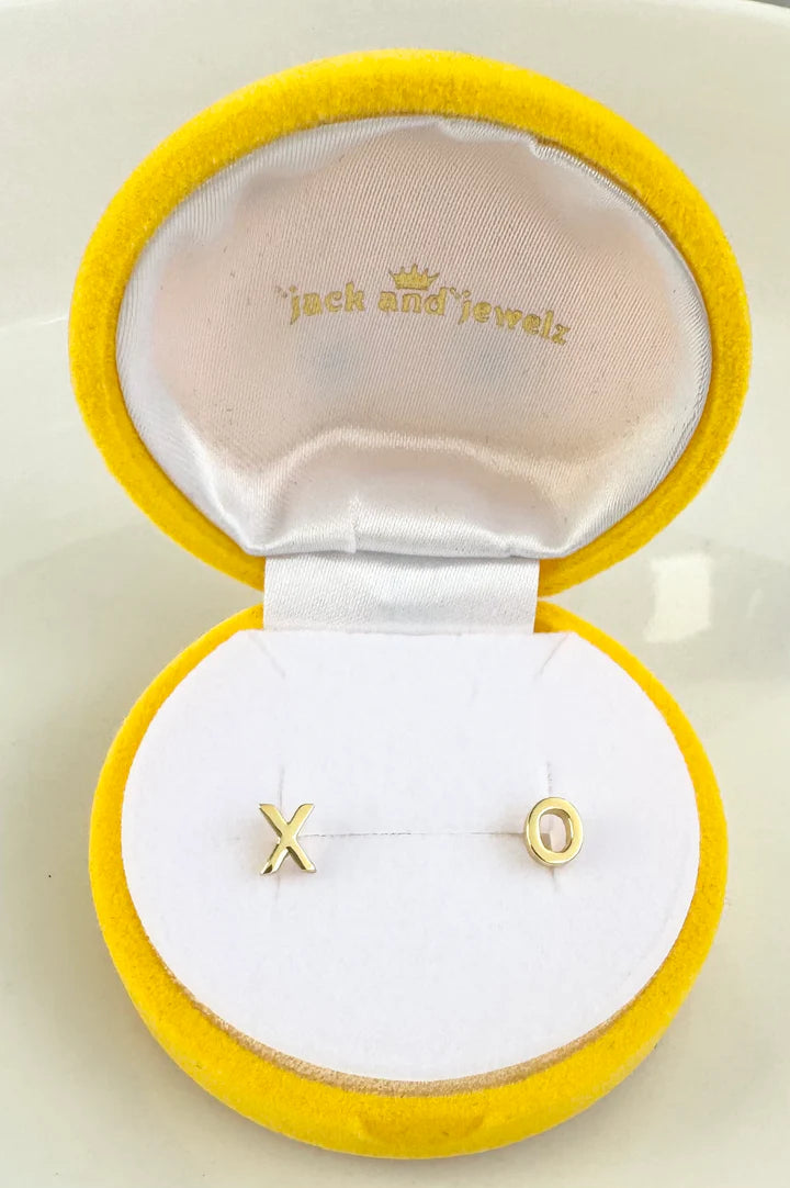 Product photography featuring Jack and Jewelz gold X and O stud earrings nestled in a bright yellow velvet jewelry box with a pristine white satin lining
