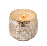 A photograph of a triple-wick candle in a textured metallic gold mercury glass holder with creamy white wax and three glowing flames