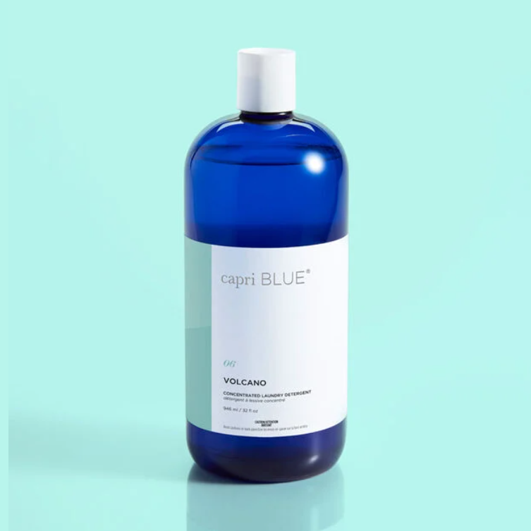 A blue bottle of Capri Blue Volcano laundry detergent on a light turquoise background.